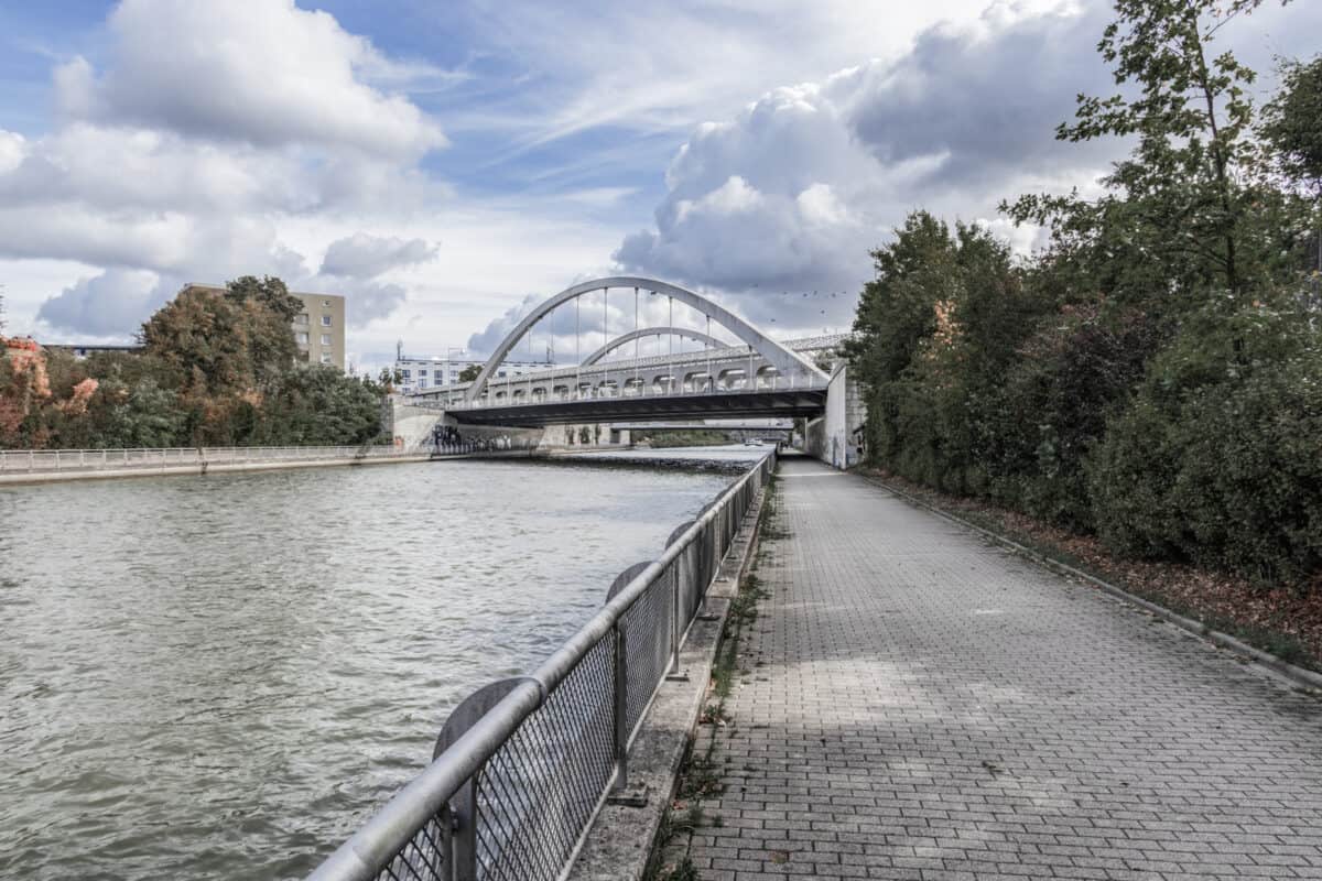 Moderne Fußgängerbrücke über die Spree in Berlin, umgeben von Bäumen und urbaner Umgebung.