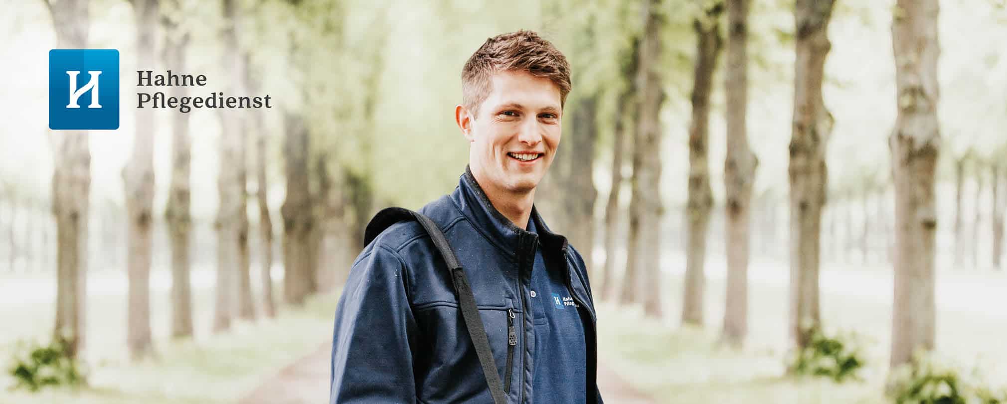 Hahne Pflegedienst, freundlicher Mitarbeiter im Freien, in blauer Arbeitskleidung, Naturumgebung, professioneller Pflegeservice.