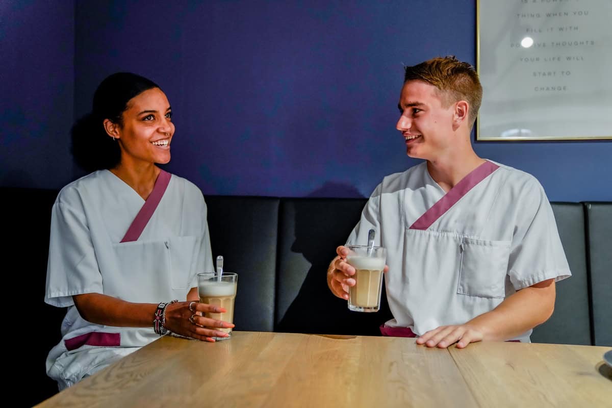 Fröhliche Pflegekräfte beim Austausch, trinken Milchshakes in modernem Bistro, Großbritannien.