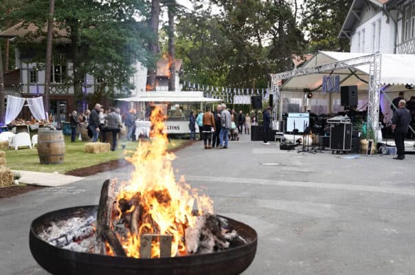 Feuerstelle im Außenbereich bei einer offenen Veranstaltung mit Zelt und Musikbühne.