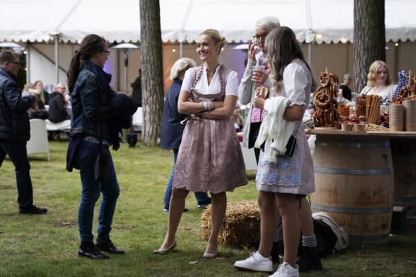 Fröhliche Menschen beim Oktoberfest in traditioneller Tracht mit Bier und Brezeln auf einem Volksfest in Deutschland.