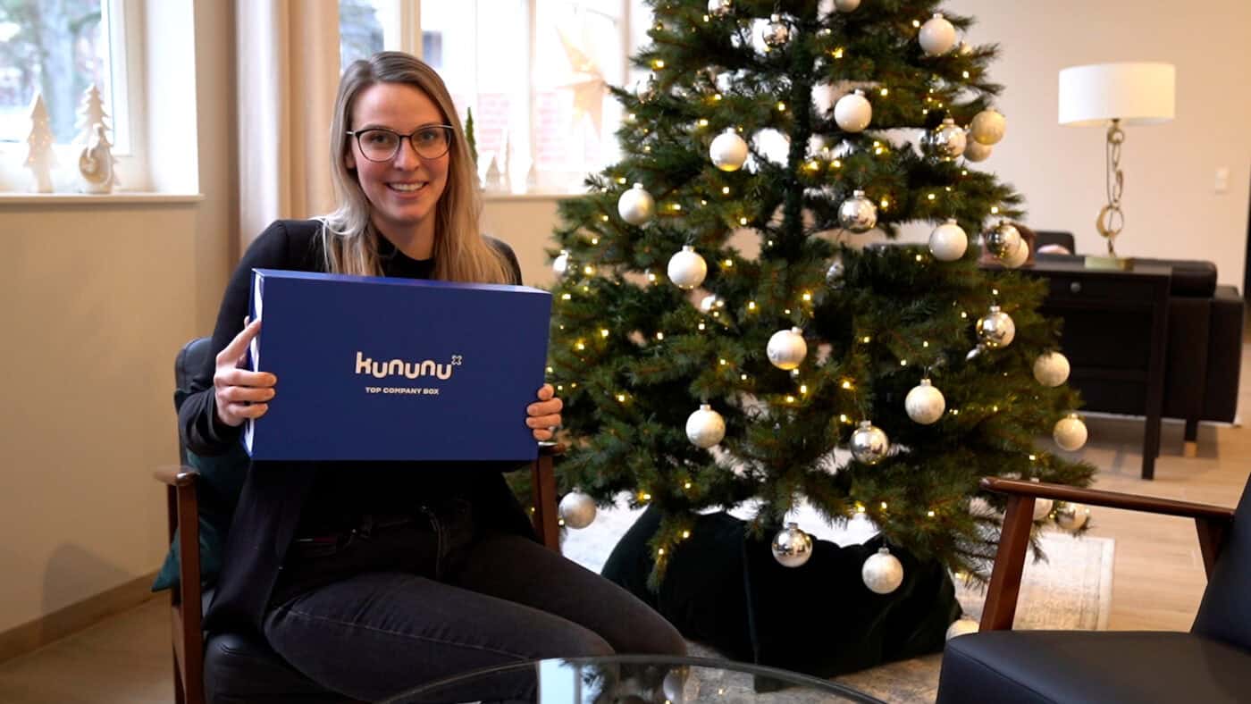 Hahne Holding, festliche Weihnachtsdeko, beschenkte Mitarbeiterin mit Firma-Box vor Weihnachtsbaum.