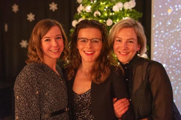 Fröhliche Frauen feiern Weihnachten vor einem festlich geschmückten Baum.
