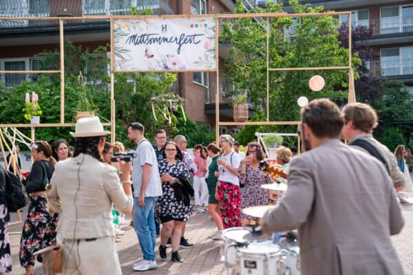 Fröhliche Menschen bei einem Sommerfest im Innenhof mit Dekorationen und Musik.
