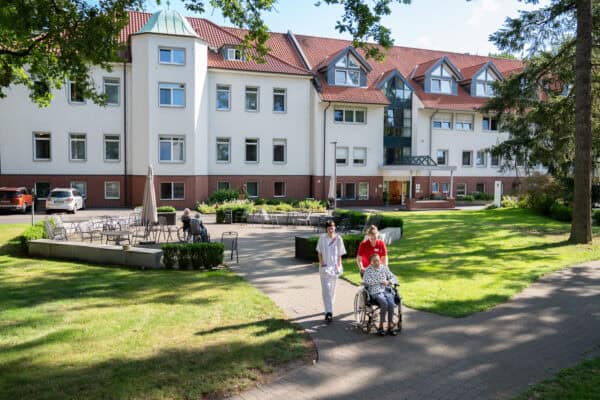 Pflegeheim Hahne Holding mit betreutem Wohnen in grüner Umgebung, Pflegekräfte und Rollstuhlfahrerin.