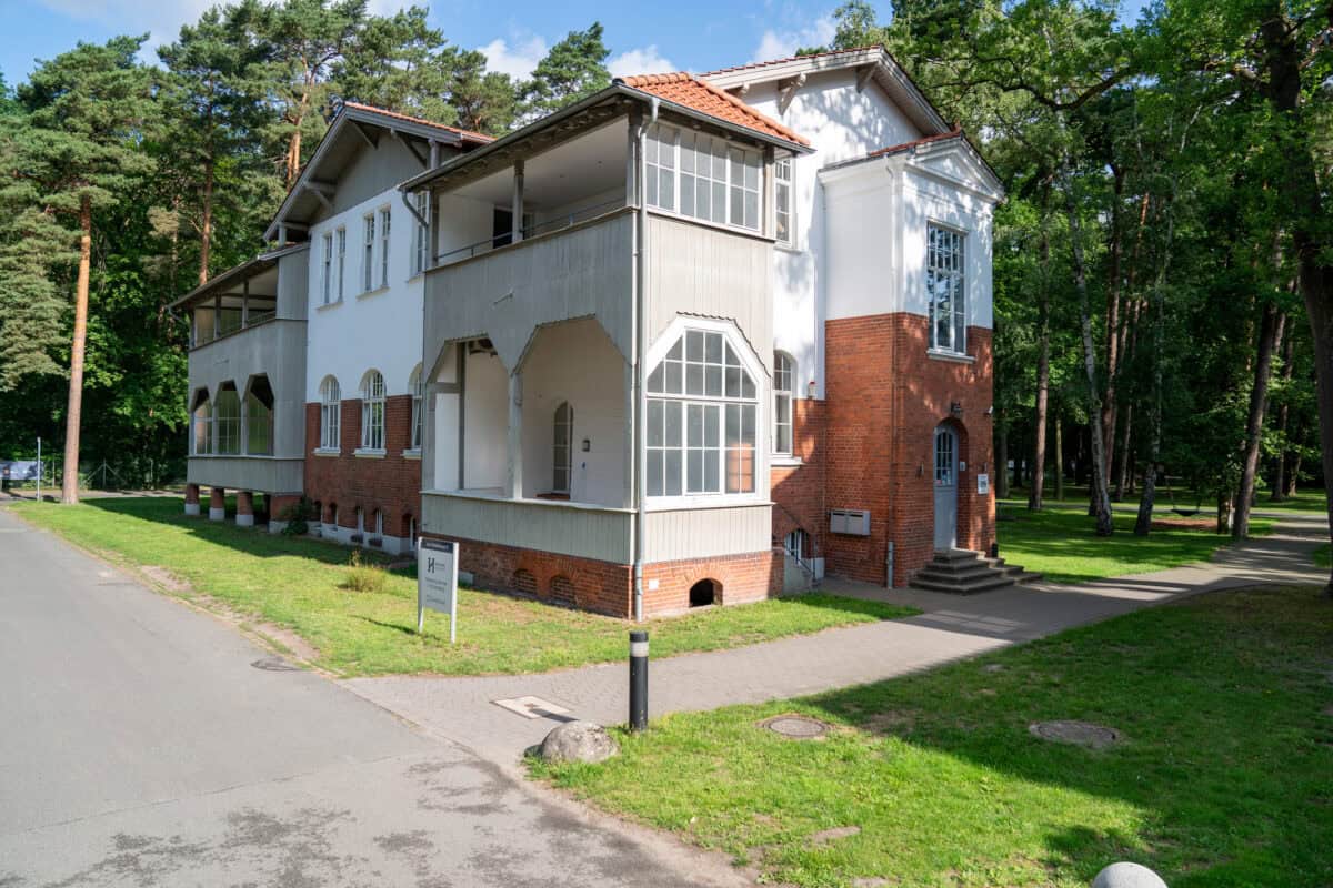 Alt: Historisches Haus mit modernen Elementen, umgeben von Bäumen und Grünfläche.