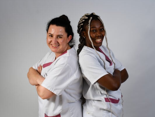 Freundliche Pflegekräfte in weißen Kitteln, lächelnd und selbstbewusst.