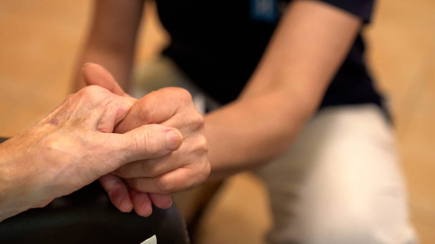 Zwei Menschen halten sich liebevoll an den Händen, symbolisiert Fürsorge und Unterstützung im Pflege- oder Betreuungskontext.